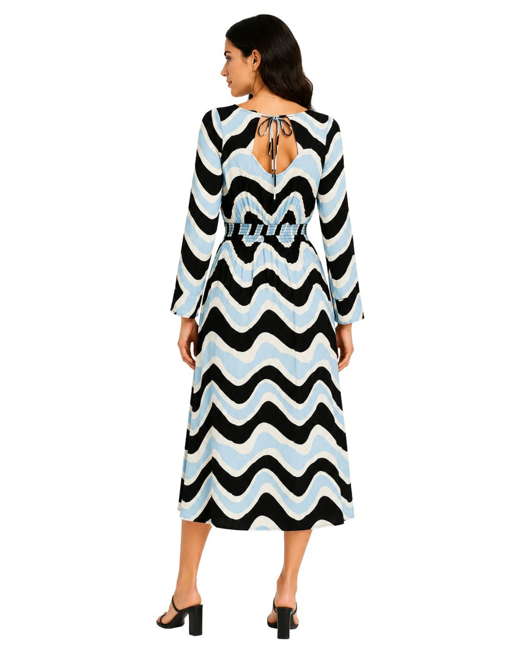 A woman viewed from the back wearing a long-sleeve midi dress with a black, white, and light blue wavy zigzag pattern and a tie detail at the neckline, paired with black heeled sandals against a plain white background.