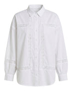 A white long-sleeve button-up shirt with decorative white lace trim outlining the chest pockets and cuffs, shown against a plain white background.