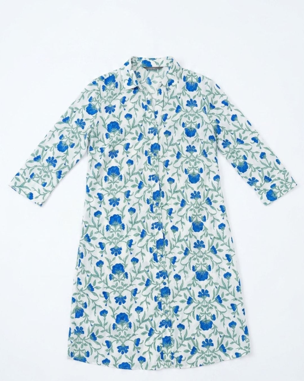 A long-sleeve button-up shirt dress with a white base and an all-over blue floral and green vine pattern, laid flat against a white background.