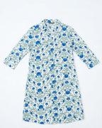 A long-sleeve button-up shirt dress with a white base and an all-over blue floral and green vine pattern, laid flat against a white background.