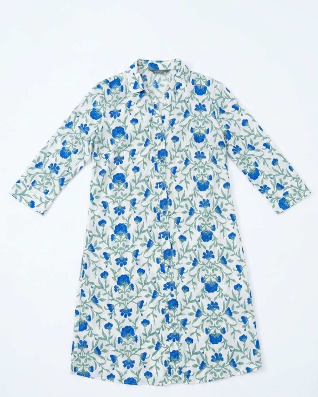 A long-sleeve button-up shirt dress with a white base and an all-over blue floral and green vine pattern, laid flat against a white background.