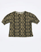 A short-sleeve crop top featuring a black and olive green snakeskin pattern, laid flat against a light gray background.