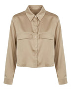 A cropped long-sleeve button-up shirt in a light beige or khaki color, featuring a pointed collar, button front, and two flap chest pockets, shown against a plain white background.