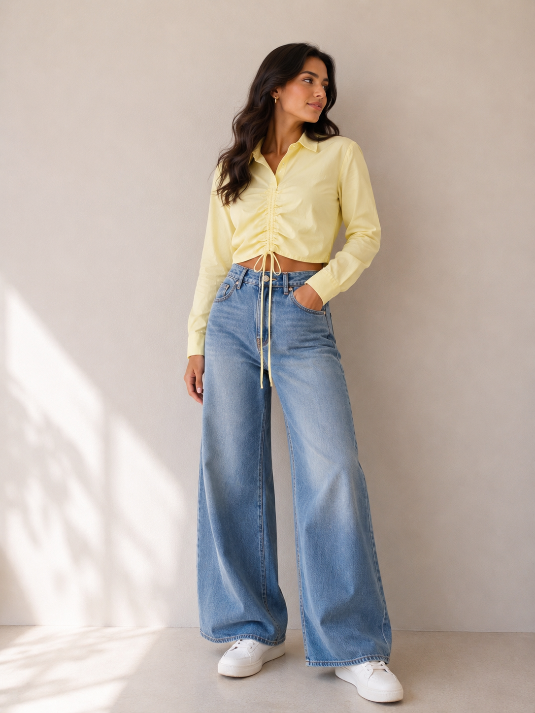 Woman wearing a light yellow shirt and blue jeans standing against a neutral background