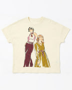 An off-white short-sleeve t-shirt featuring a graphic print of two retro-style illustrated women, one in a pink and maroon outfit and the other in a yellow-green dress, both wearing patterned neckties.