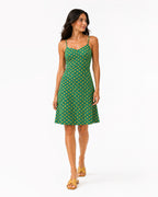 A woman modeling a green sleeveless midi dress with a yellow geometric pattern, standing against a plain white studio background.