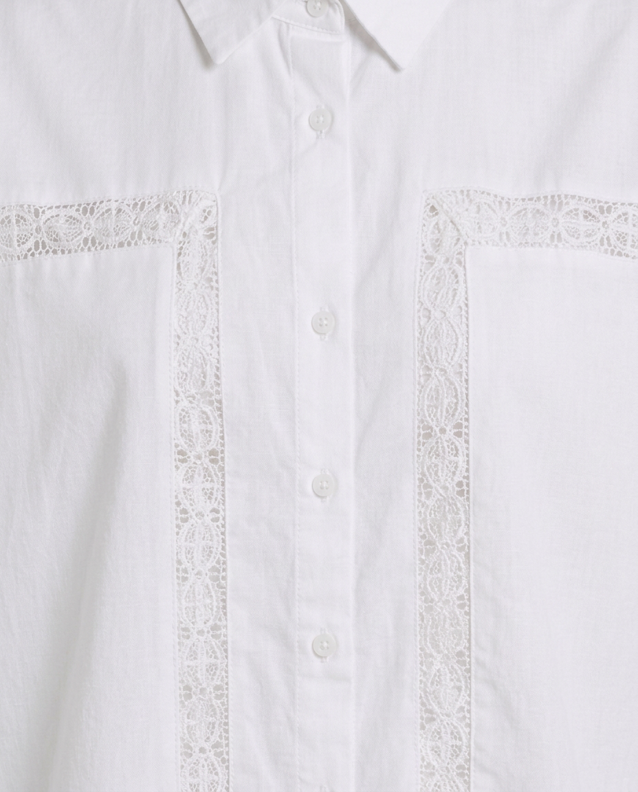 Close-up of a white button-front shirt with decorative lace trim running vertically on the chest and across the pocket edges.