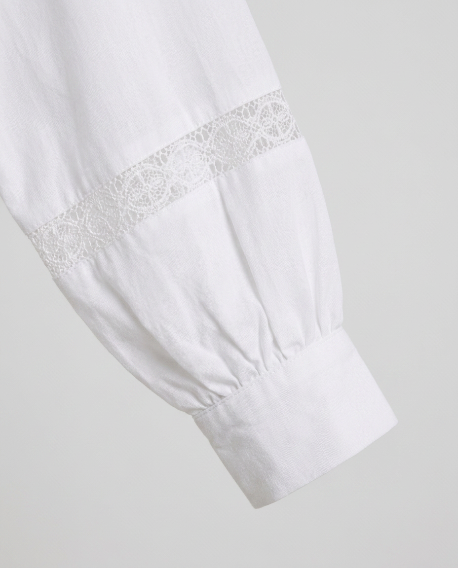 Close-up of a white long-sleeve blouse or dress sleeve with gathered cuffs and a decorative white lace band near the upper cuff, shown on a light gray background.