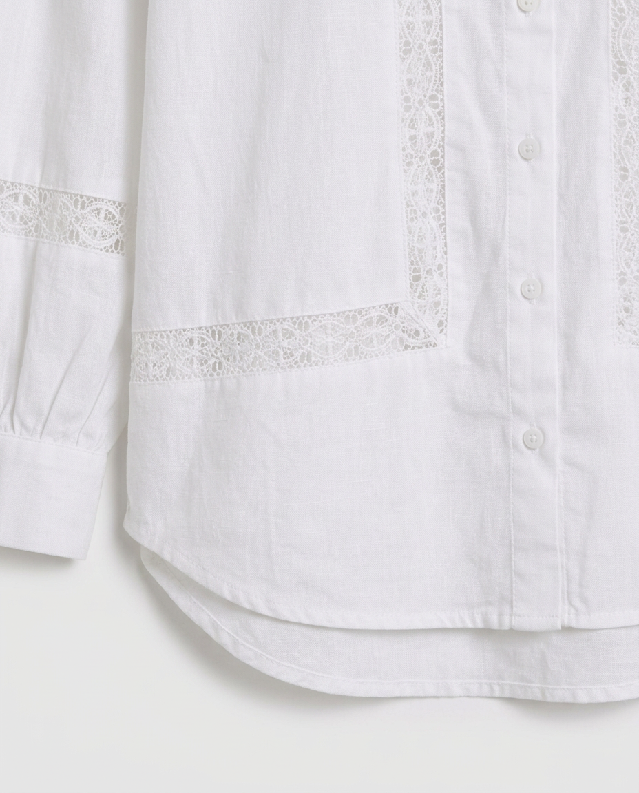 Close-up of a white button-front shirt with delicate lace trim along the pocket edges and sleeve cuff, shown against a plain light background.