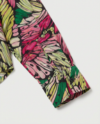 Close-up of a long-sleeve shirt sleeve with a bold abstract floral or leaf-like print in pink, lime green, yellow, and black on a light gray background.