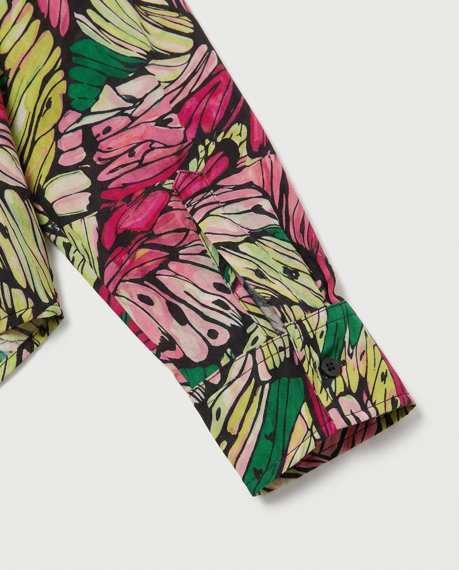 Close-up of a long-sleeve shirt sleeve with a bold abstract floral or leaf-like print in pink, lime green, yellow, and black on a light gray background.