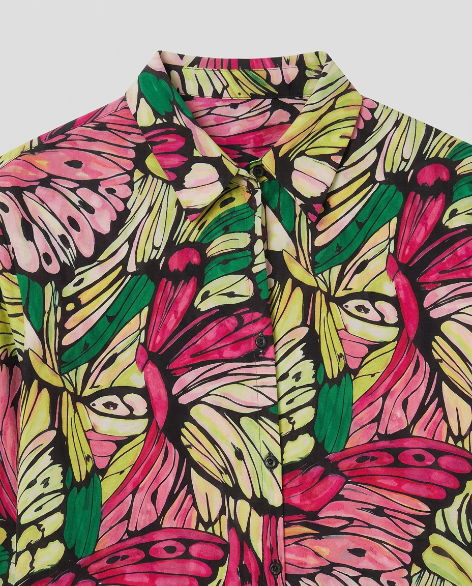 A close-up of a button-up shirt featuring a vibrant, hand-drawn butterfly and leaf pattern in pink, green, and yellow on a black background.