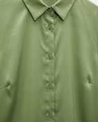 Close-up of a light olive green button-down shirt showing the collar, front buttons, and fabric texture.