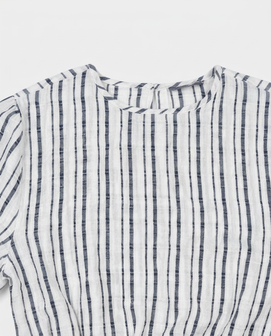 A close-up of a white cotton gauze top with vertical navy blue stripes, showing the textured fabric and collar detail.