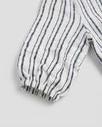 A close-up of a white fabric garment with vertical dark gray stripes and an elasticized cuff, shown on a light gray background.