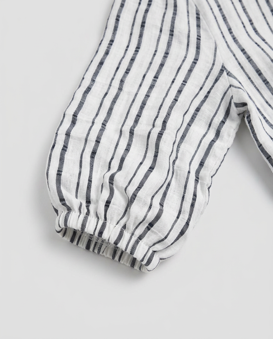 A close-up of a white fabric garment with vertical dark gray stripes and an elasticized cuff, shown on a light gray background.