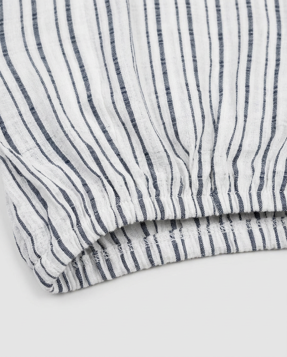Close-up of a striped fabric product, showing vertical navy blue stripes on a white textured material, folded to reveal the weave and hem.