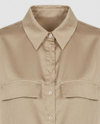 A close-up of a beige button-up shirt with a pointed collar and two chest flap pockets, shown against a light gray background.