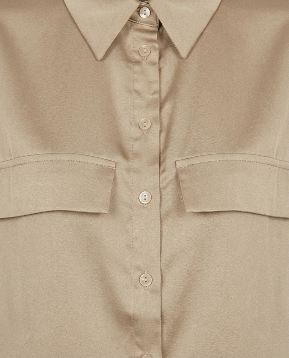 Close-up of a beige button-up shirt with a pointed collar, matching buttons, and two chest flap pockets.