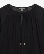 A close-up of a black pleated blouse with a gathered round neckline, a front tie closure, and small metallic gold ring accents near the center front.