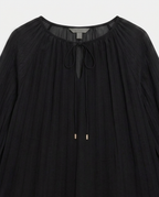 A black pleated long-sleeve blouse with a round neckline, sheer mesh trim, and a front tie closure with small gold-toned bead accents.