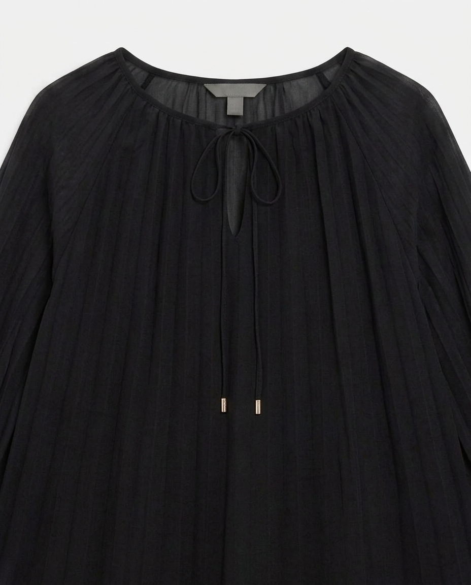 A black pleated long-sleeve blouse with a round neckline, sheer mesh trim, and a front tie closure with small gold-toned bead accents.
