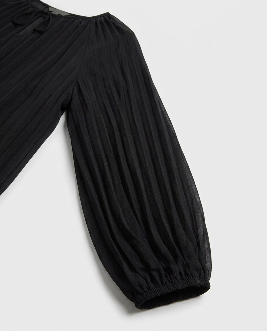 Close-up of a black pleated garment with a gathered elastic cuff, shown against a light gray background.