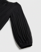 Close-up of a black pleated garment with a gathered elastic cuff, shown against a light gray background.