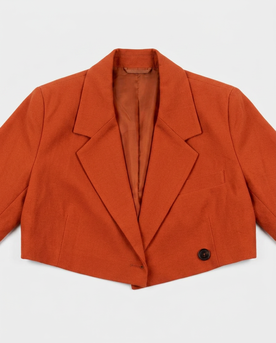 A cropped orange-brown blazer with notched lapels and a single visible dark button, laid flat against a light gray background.