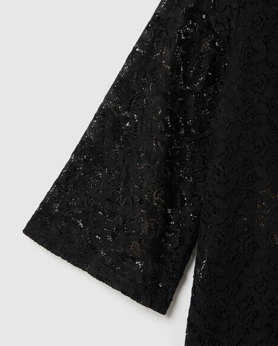 Close-up of a black lace garment sleeve with sheer floral embroidery and subtle shimmer, shown against a light gray background.